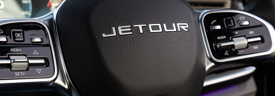 Close-up of a Jetour steering wheel, showcasing the brand logo and control buttons for various functions.