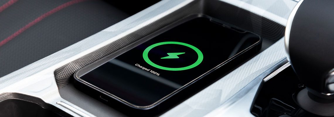 Smartphone on a car's center console wirelessly charging, display shows a green circle with a lightning bolt, indicating 100% charged.